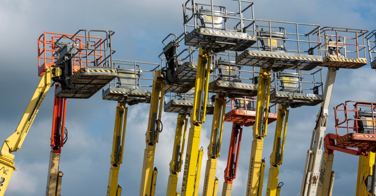 Multiple aerial work platforms with colorful booms reaching skyward against a cloud-dotted backdrop.